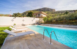 Una piscina con sillas de descanso, vista despejada de una montaña y un edificio al fondo.