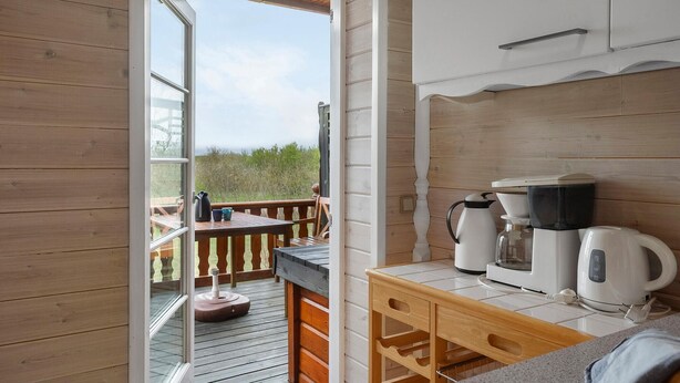 Terraza de madera con una mesa y sillas, una estación de café con hervidores y tazas, y vistas al exterior.