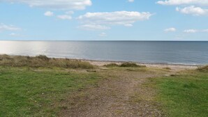 Un sendero costero que lleva a una playa, con vista despejada al mar y al cielo.