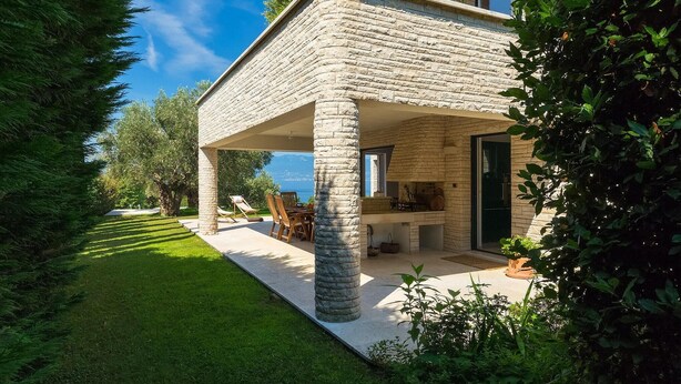 A stone house with a covered patio, a dining area, and a view of the sea.