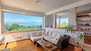 A modern living room with a large window, a sectional sofa, a coffee table, and a bookshelf.