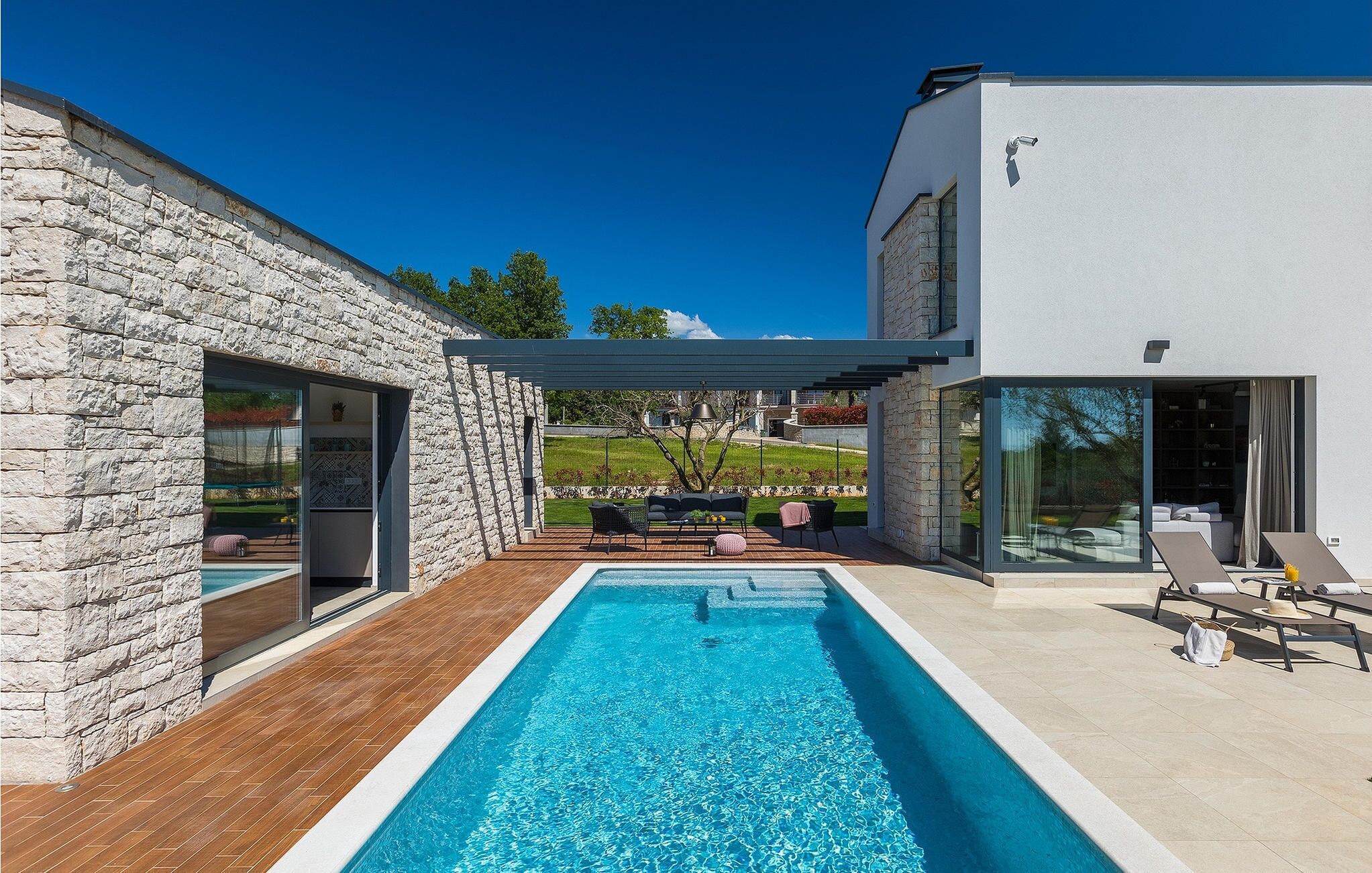 Ein modernes Haus mit Swimmingpool, Steinmauern und einer Terrasse mit Gartenmöbeln.