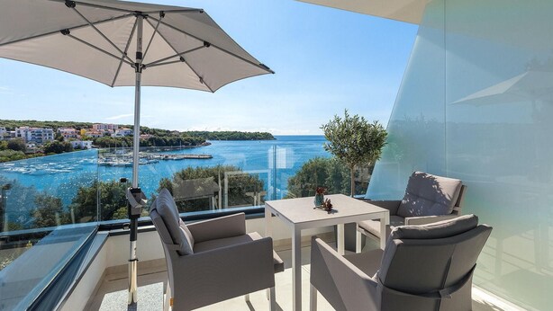 A balcony with a table and chairs, a large umbrella, and a view of a marina and sea. - Beautiful home in Pula (Pula)