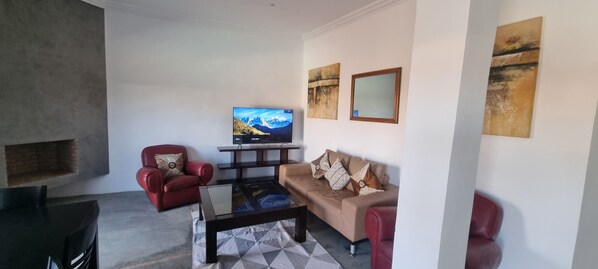 A living room with a TV, red chairs, a sofa, and artwork on the walls.