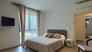 Une chambre à coucher moderne, dotée d’un grand lit, d’un téléviseur fixé au mur et offrant une vue sur l’extérieur par la fenêtre.