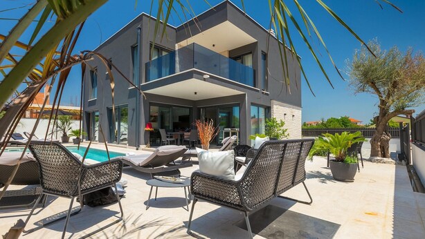 Une maison moderne à deux étages dotée d’un balcon, d’une piscine et d’un espace salon extérieur.