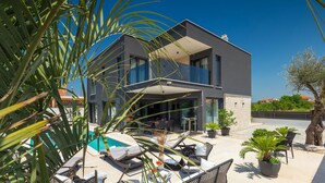 Une maison moderne à deux étages, dotée d’une piscine, d’un espace salon extérieur et de plantes en pot.