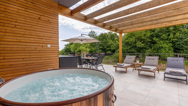 A wooden deck with a hot tub, outdoor seating, and a pergola.