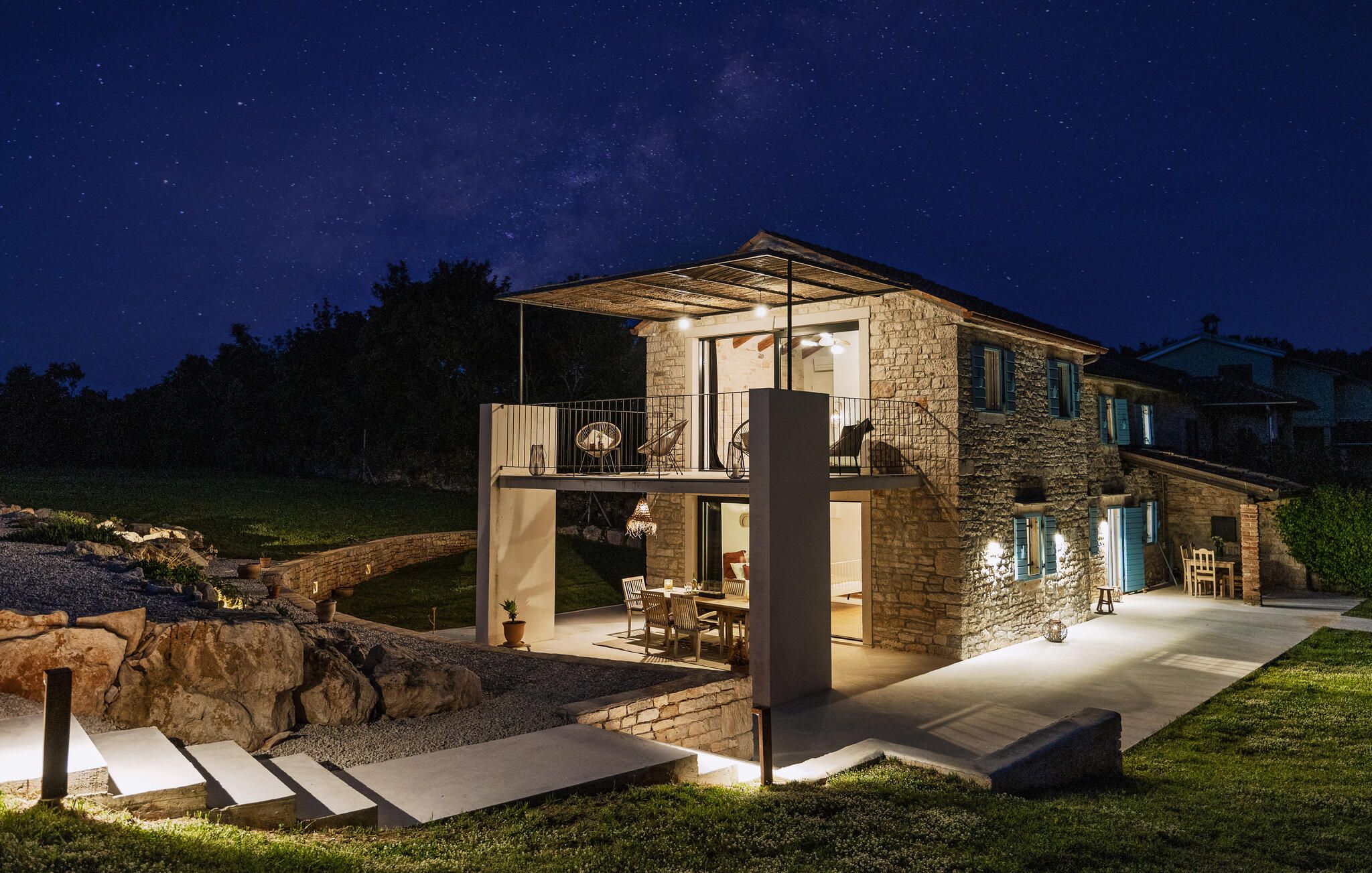 A modern house with a stone facade, a balcony, and a patio area with outdoor furniture.