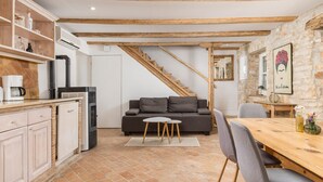 A cozy kitchen with a built-in stove, a dining area with a wooden table and chairs, a grey sofa, and a staircase leading to another level.