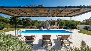 A swimming pool with lounge chairs, a covered patio, and a stone house in the background.
