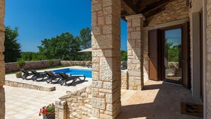 A stone patio with a pool, lounge chairs, and a wooden pergola.
