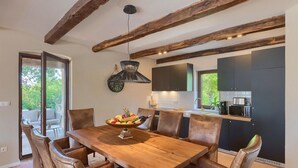 A dining area with a wooden table and leather chairs, a kitchen with dark cabinets and a microwave, and exposed wooden beams on the ceiling.