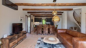 A living room with a TV, wooden furniture, a dining area, and a staircase.