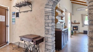 A rustic interior with exposed stone walls, a wooden table, a kitchen area with a stone fireplace, and a view through an archway. - Stunning home in Pula (Pula)