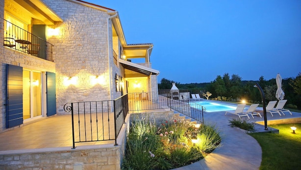 Une maison en pierre à deux étages, dotée d’une piscine, d’un espace extérieur aménagé et d’un jardin bien éclairé.