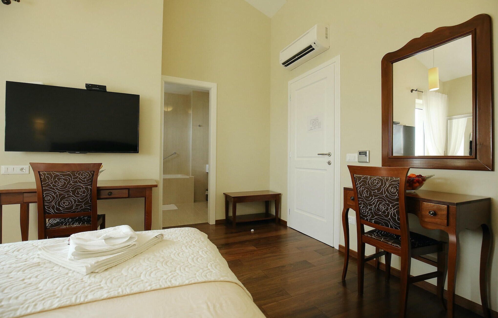 A hotel room with a bed, a desk, a chair, a television, a mirror, and an air conditioning unit.