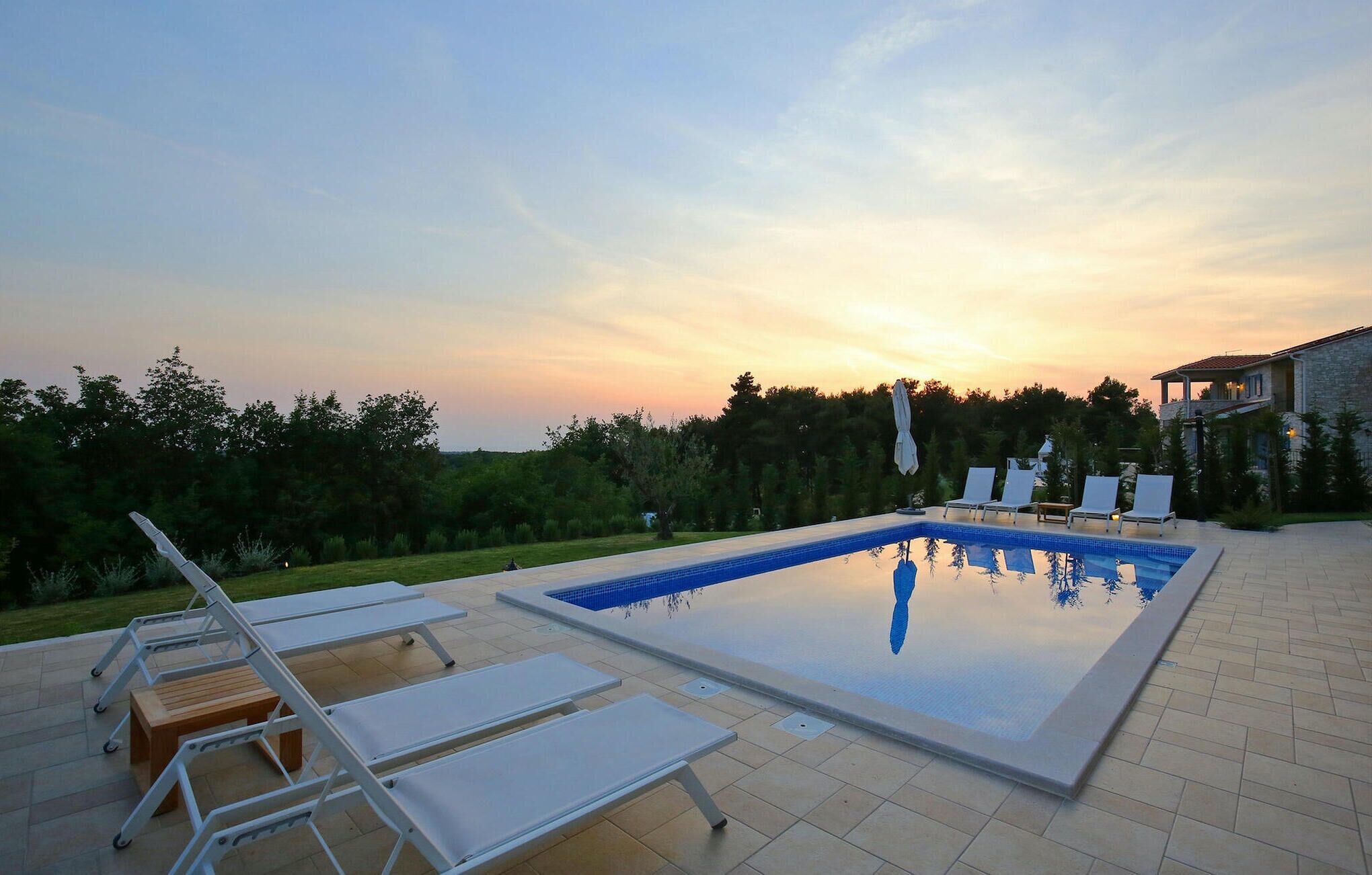 A rectangular swimming pool with clear blue water, surrounded by lounge chairs and a wooden table.