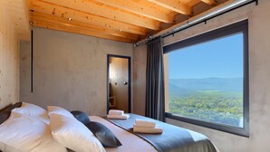 A bedroom with a large window, wooden ceiling, and a bed with pillows and towels.