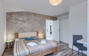 Ein modernes Schlafzimmer mit einem großen Bett, Nachttischen, einem Sessel und einem Kleiderschrank.