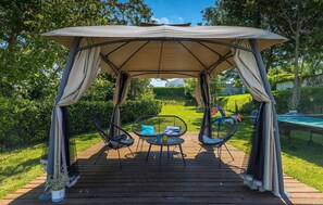 Eine Holzterrasse mit Baldachin, zwei Korbstühle und einem kleinen Tisch.