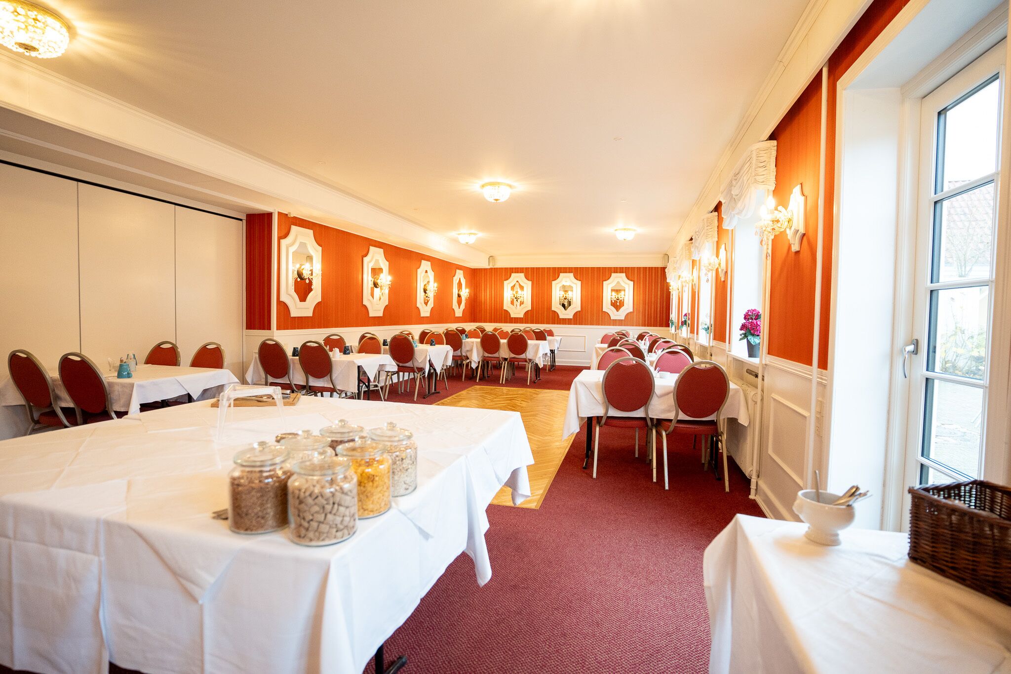 Un salón de banquetes con mesas dispuestas para comer, alfombra roja y apliques en las paredes.
