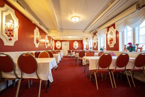 Un salón de banquetes con filas de mesas y sillas, candelabros y espejos decorativos.