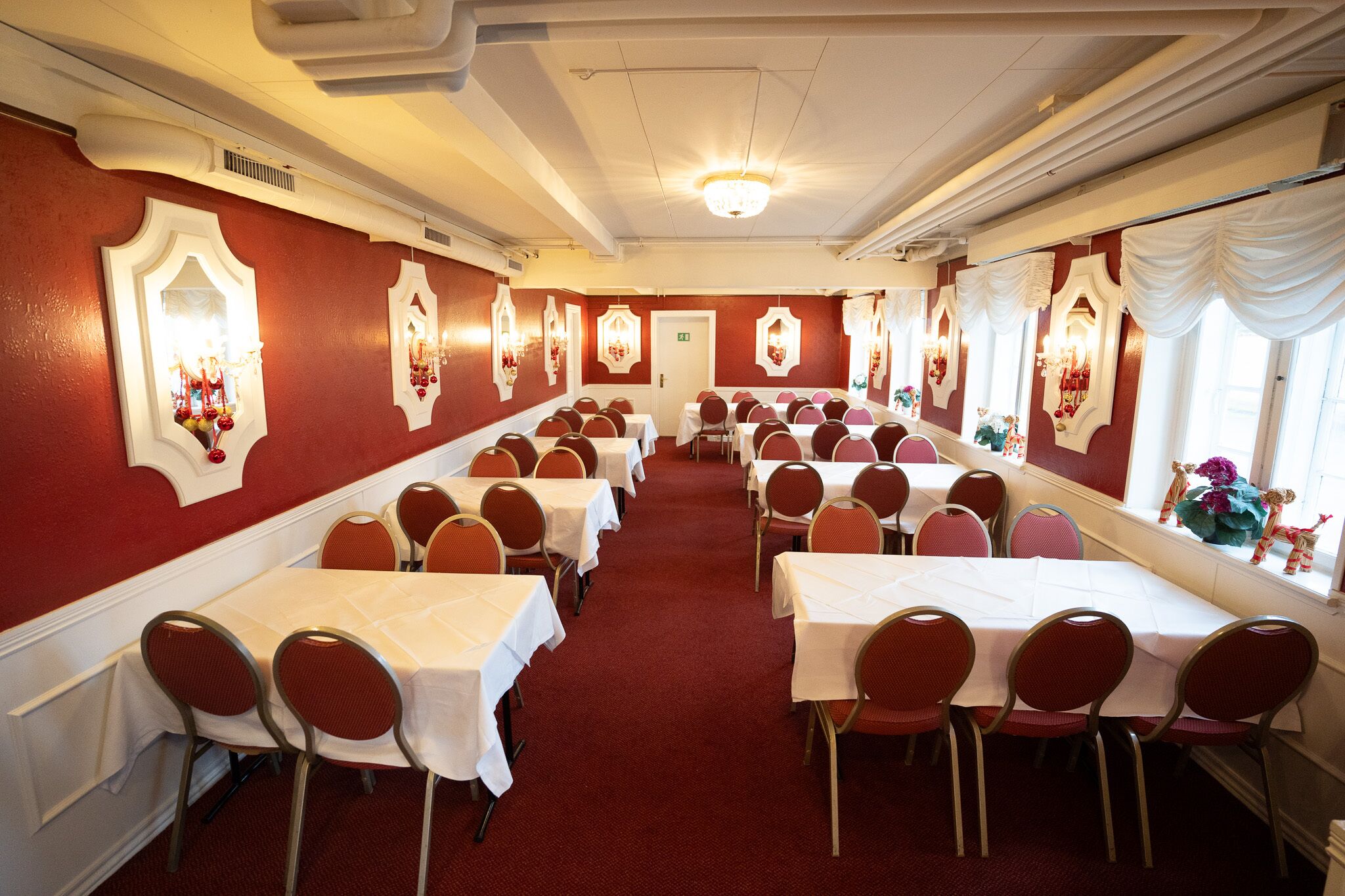 A banquet hall with rows of tables and chairs, red walls, and decorative wall sconces.