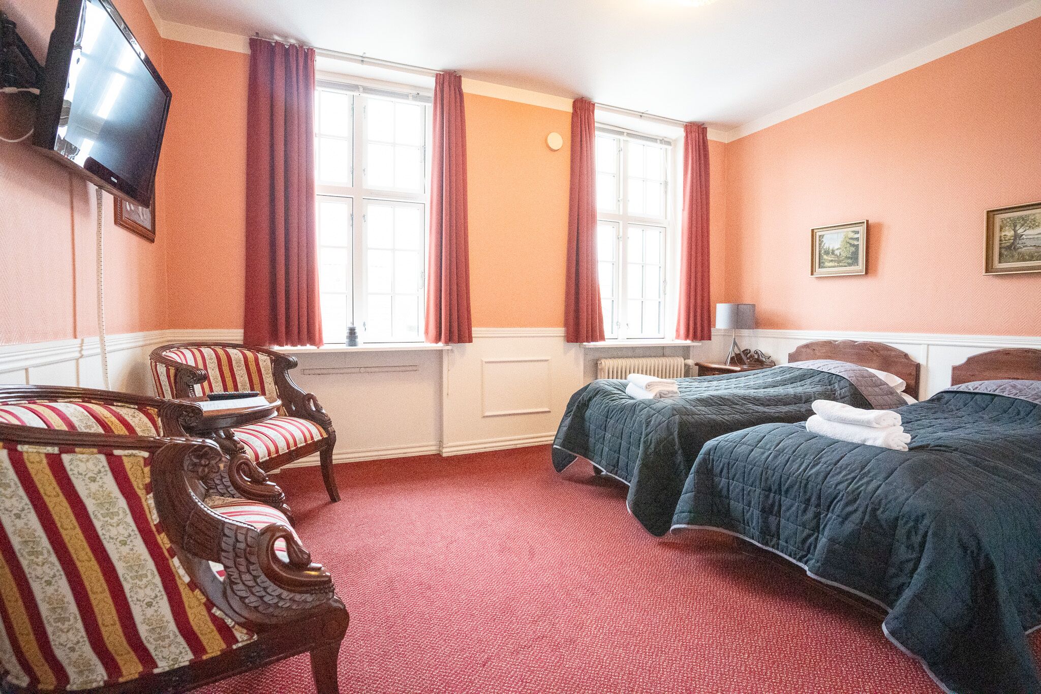 A hotel room with two beds, a TV, and a window with curtains.