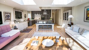 A spacious living area with a central island, a kitchen in the background, and a dining area with a white table and chairs.