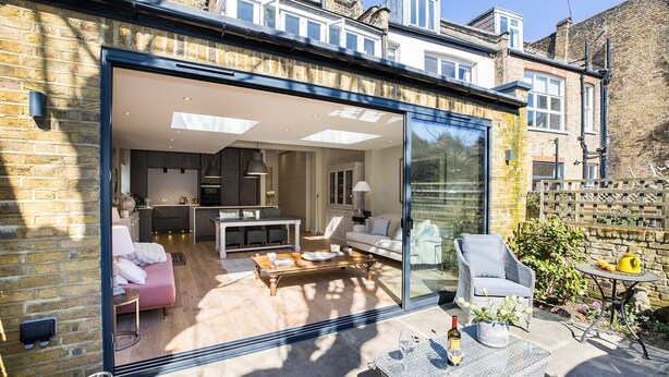 A modern home with a glass sliding door leading to a spacious living area, a kitchen, and a patio with outdoor furniture.