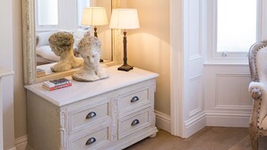 A white vanity with a large mirror, two lamps, and bust sculptures.
