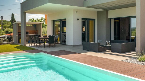 A modern outdoor pool area with a wooden deck, a dining table with chairs, and a seating area with sofas. - Gorgeous home in Buje (Buje)