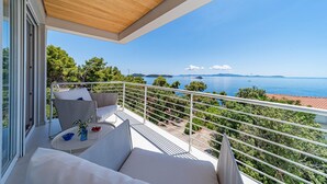 A balcony with a white sofa, a small table with a glass of water and a bowl of fruit, and a view of the sea and distant islands. - Lovely home in Blato with sauna (Blato)