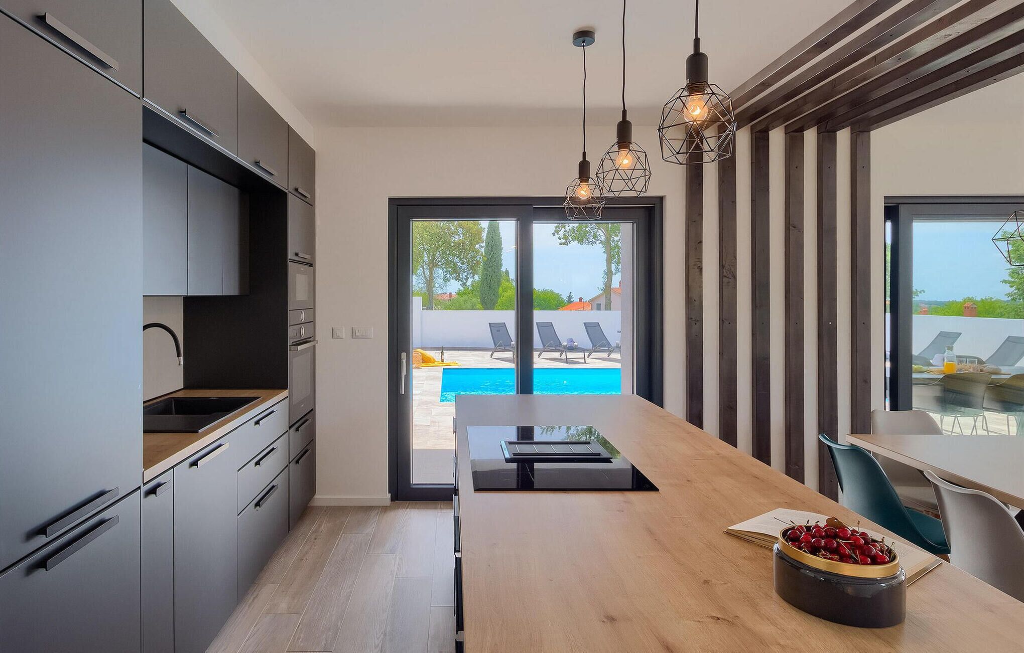 A modern kitchen with a wooden countertop, a dining area with a view of a pool, and a dining table with chairs.