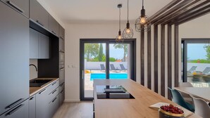 A modern kitchen with a wooden countertop, a dining area with a view of a pool, and a dining table with chairs. - Amazing home in Barban (Barban)