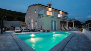 Una casa moderna de dos pisos amb piscina, mobiliari d'exterior i una xemeneia.