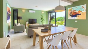 Een moderne woonkamer met een eethoek, groene wanden, een groot raam en een flatscreen televisie.