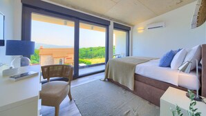 Een slaapkamer met een bed, een stoel, een bureau en een groot raam met uitzicht op het omliggende landschap.