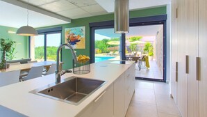 Een moderne keuken met een groot schiereiland, een roestvrijstalen spoelbak en uitzicht op een zwembad en terras.