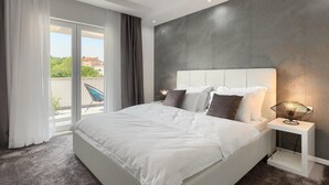A modern hotel room with a large bed, a bedside table with a lamp, and a view of the outdoors.