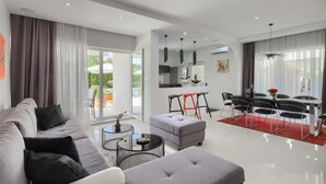 A modern living room with a grey sofa, a round coffee table, and a dining area with black chairs and a red rug.