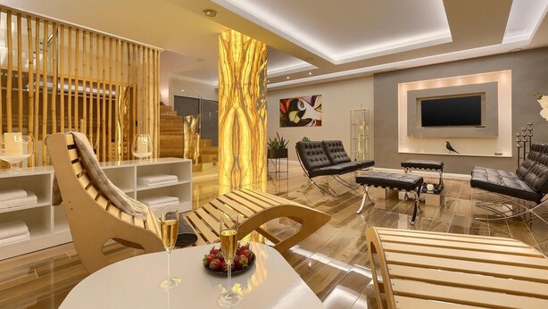 A modern living room with a wooden staircase, a large TV mounted on the wall, and a seating area with sofas and a coffee table.