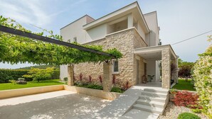 A modern two-story house with a stone facade, a covered porch, and a well-maintained garden.