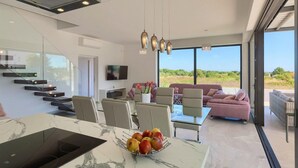 A modern kitchen with a marble countertop, a dining area with a glass table, and a living area with a pink sofa and a TV. - Gorgeous home in Pula with sauna (Pula)