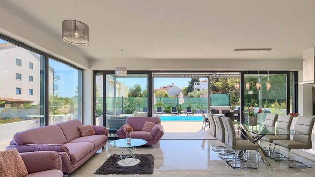 A modern living room with a glass door leading to a pool area, furnished with sofas and a glass table. - Gorgeous home in Pula with sauna (Pula)