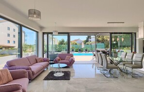 Una sala de estar moderna con puerta de vidrio que da a una zona de piscina, amueblada con sofás y una mesa de vidrio.