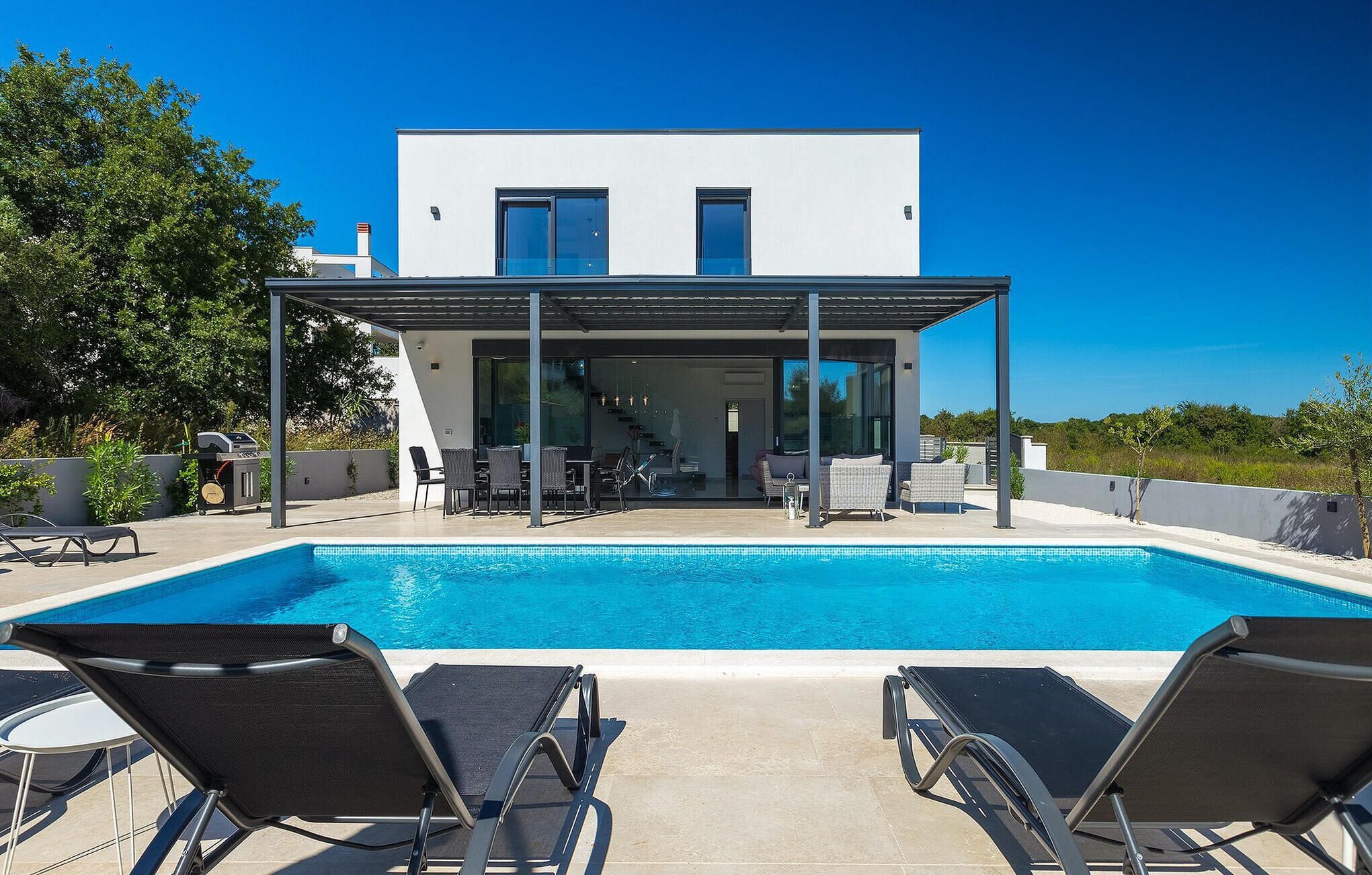 A modern house with a pool, outdoor seating, and a covered patio.