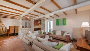 A spacious living area with a stone wall, wooden beams, and a green painting.