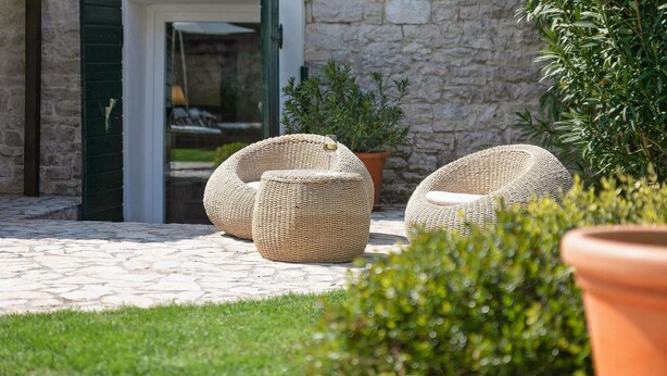 A stone building entrance with a glass door, two wicker chairs, and a potted plant.